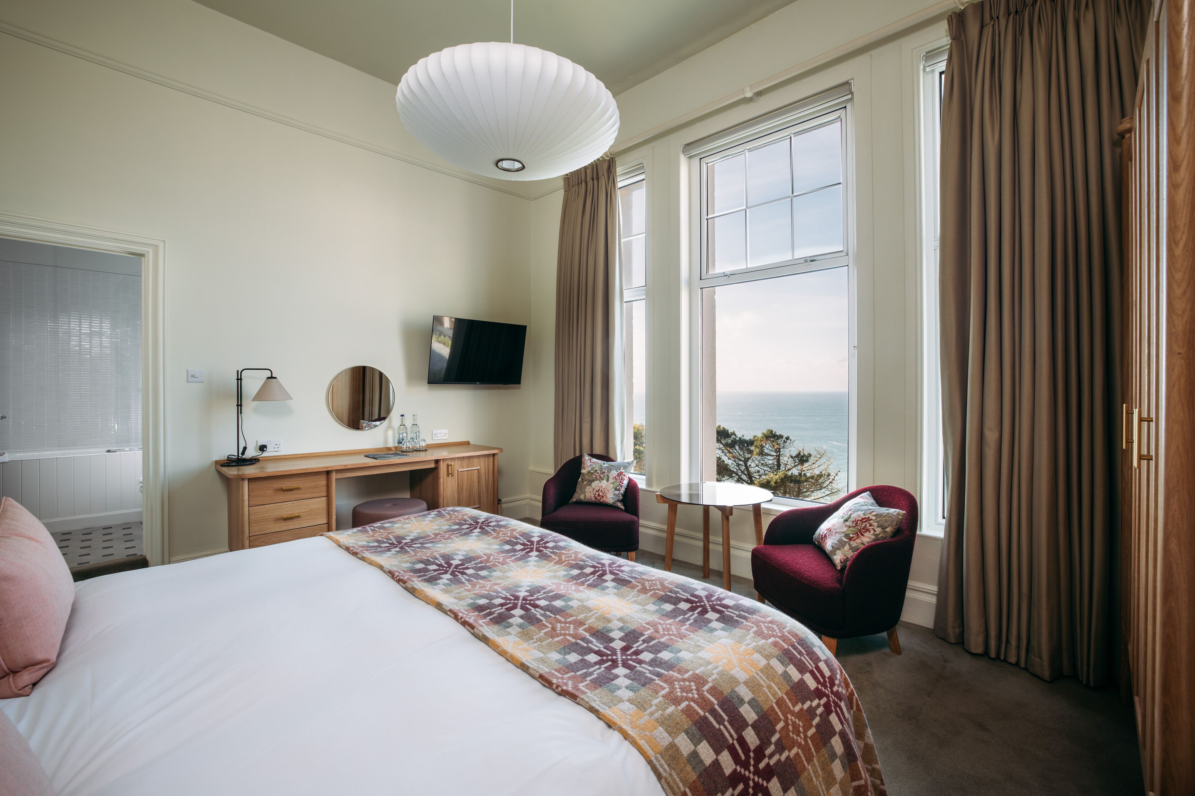 A hotel room with a bed, desk, chair, and a large window offering a view.