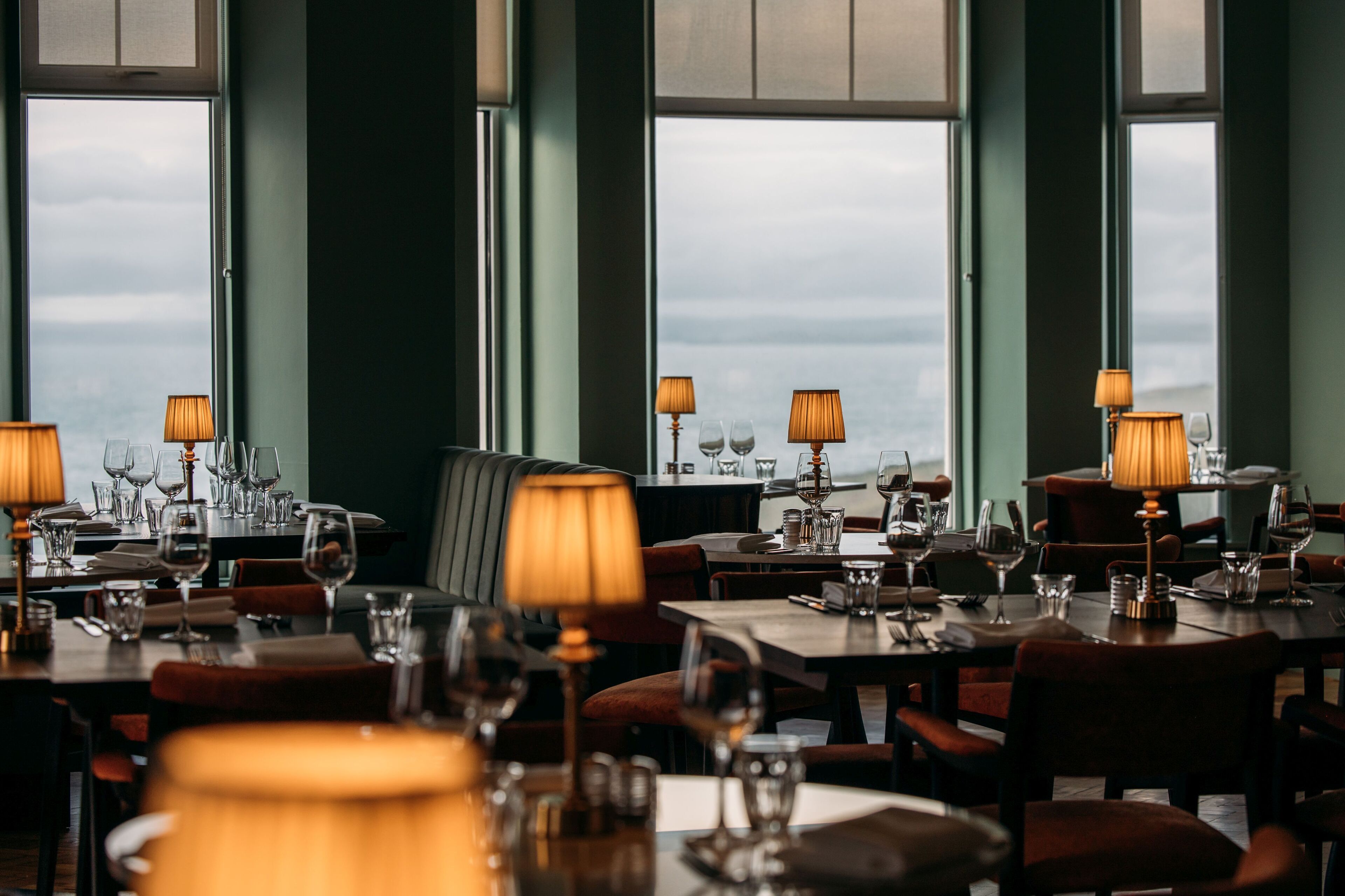 A restaurant with tables set for dining, each with a lamp and wine glasses.