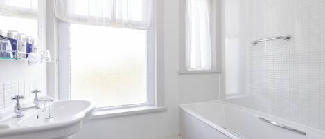 A bathroom with a white sink, a bathtub, and a window with sheer curtains.