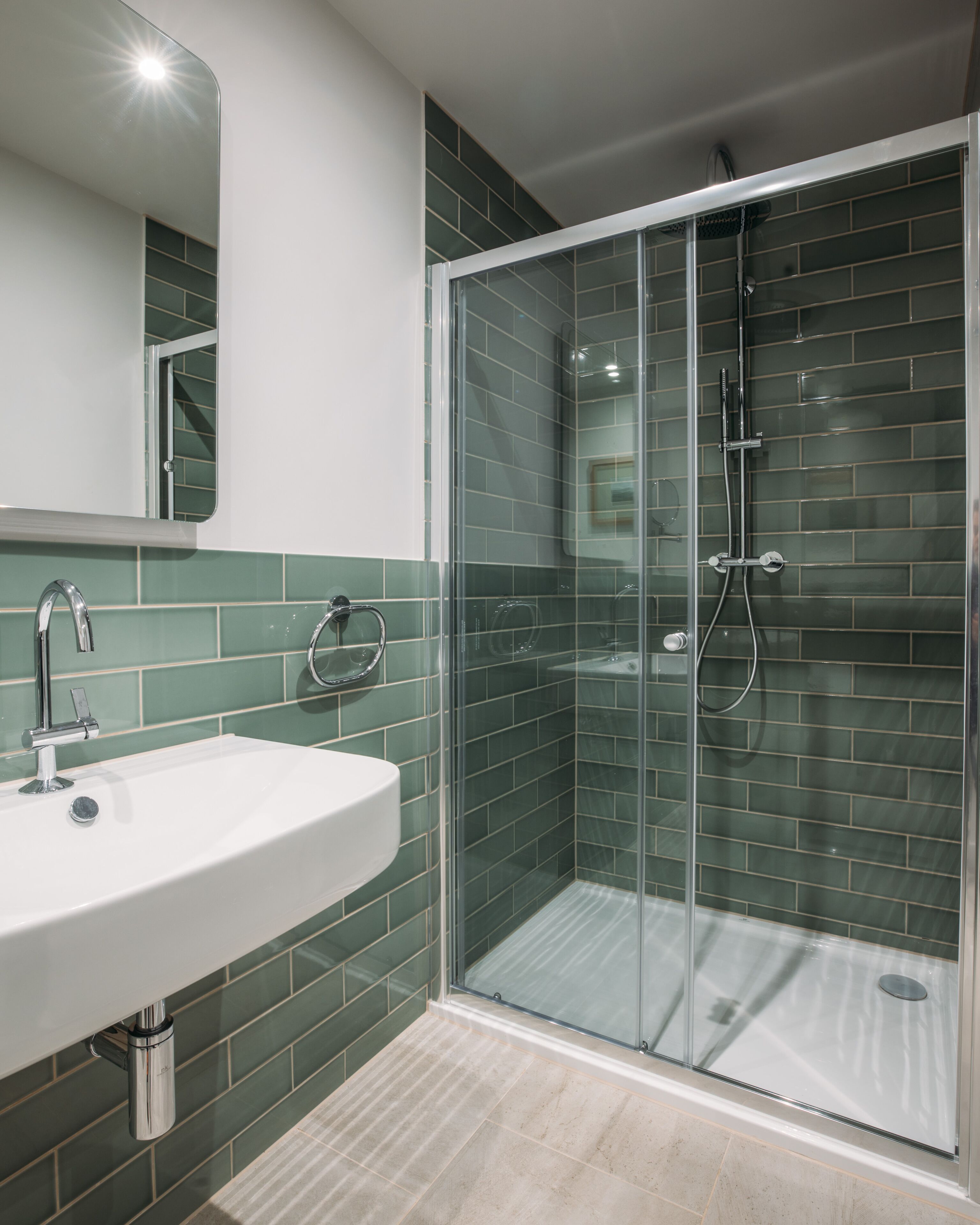 Un baño moderno con cabina de ducha de vidrio, un lavabo blanco y paredes con azulejos verdes.