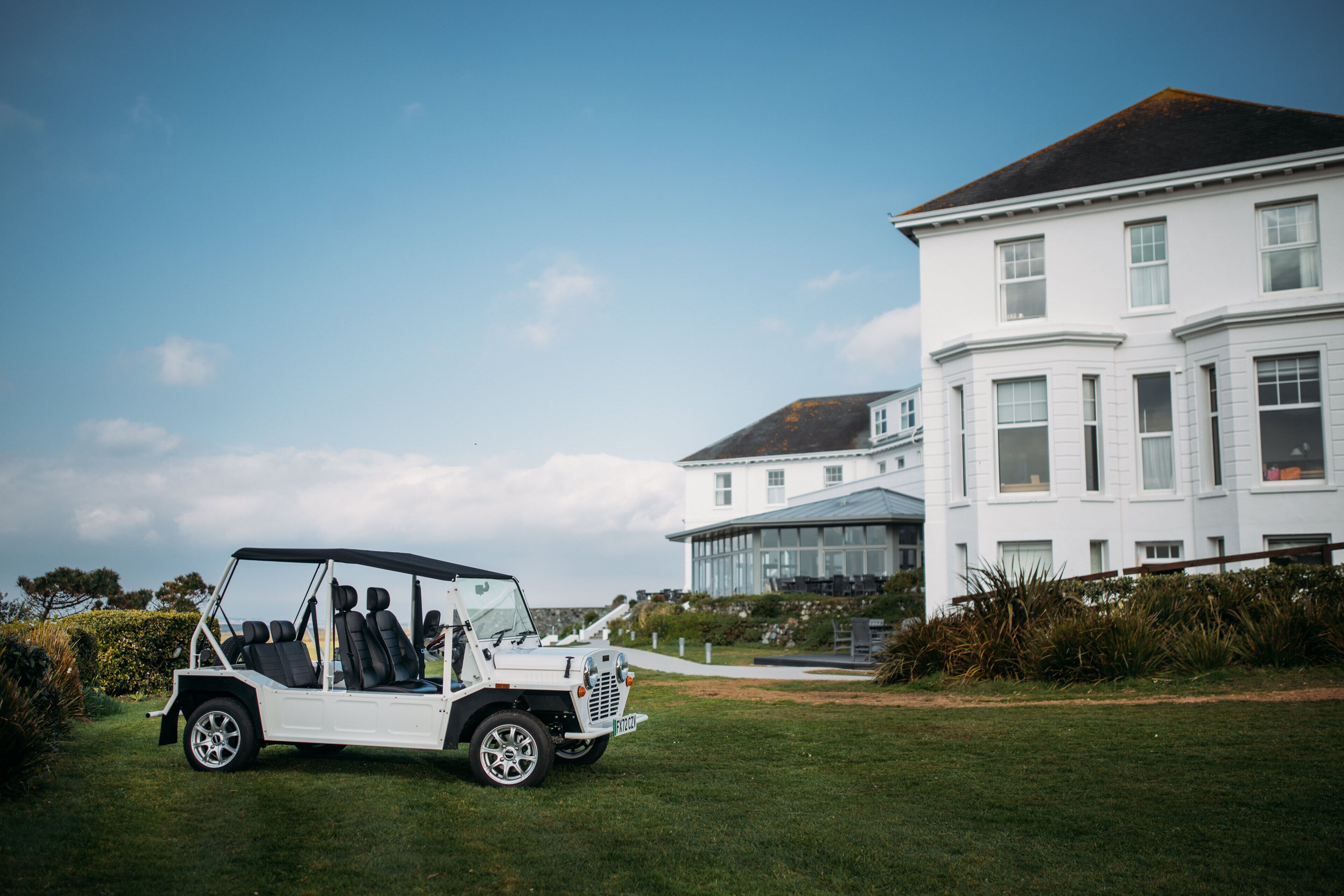 A white golf cart parked on a grassy area in front of a large white building with multiple windows and a glass entrance.
