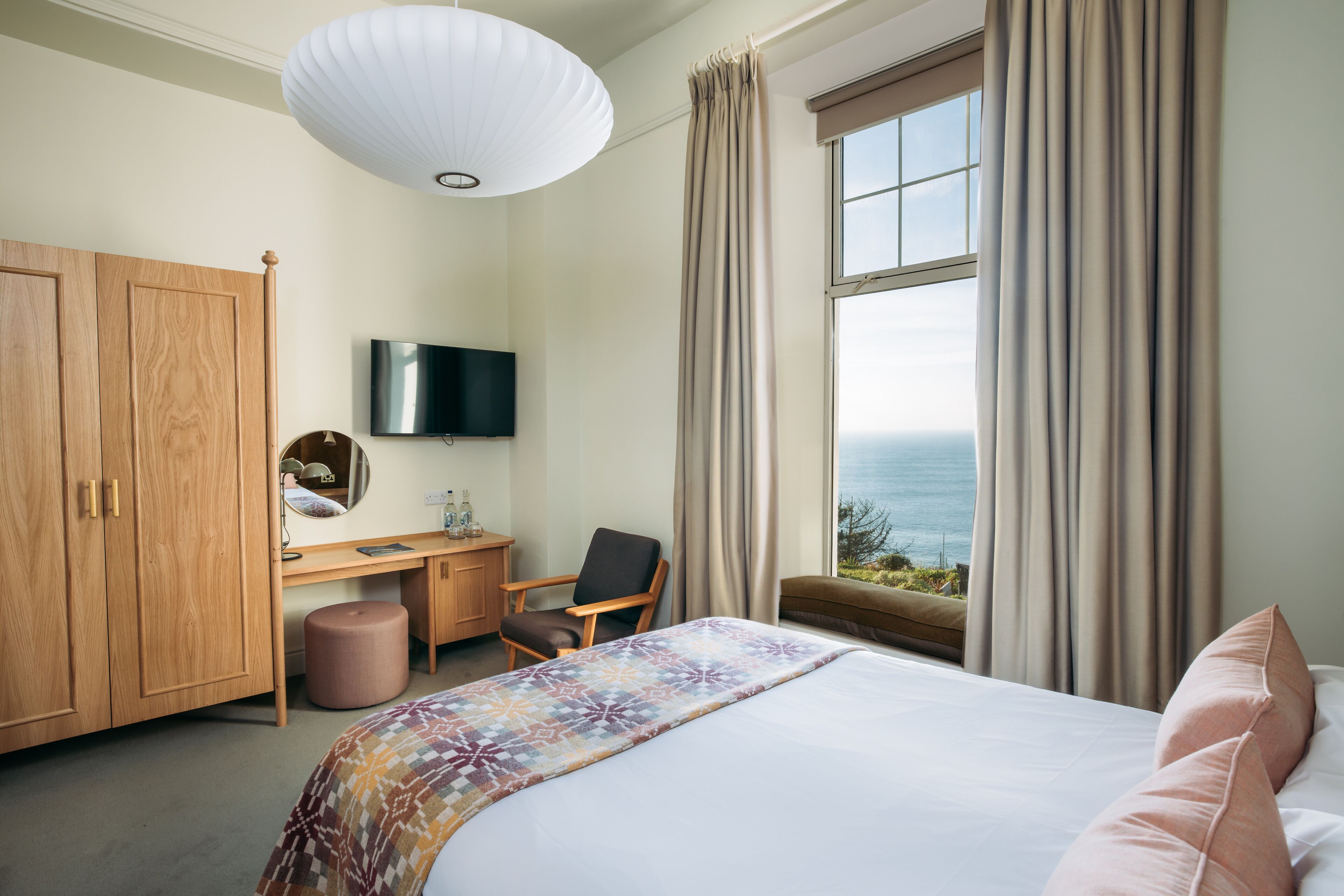 Una habitación de hotel con cama, escritorio, silla, televisión y vista al océano.