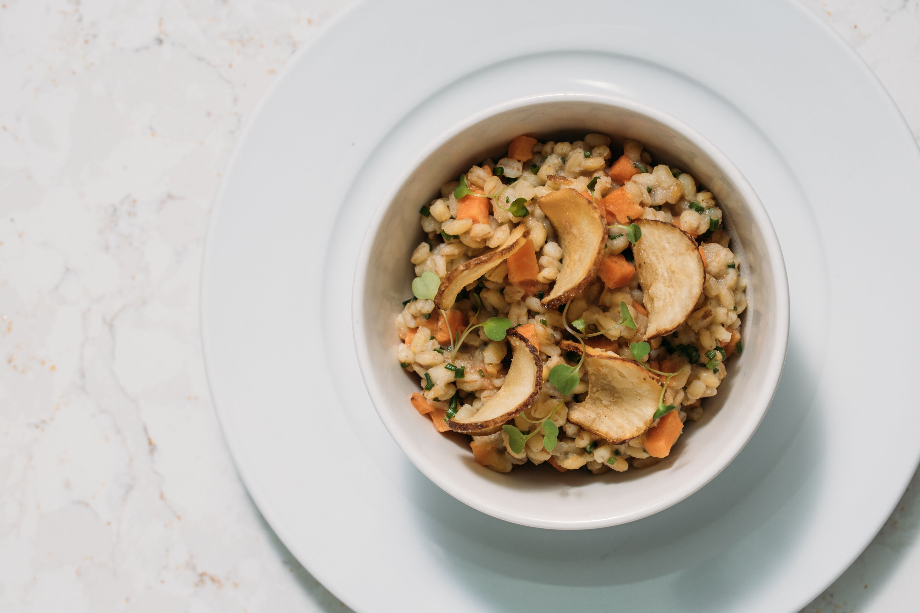 A bowl of grain-based dish with vegetables and mushrooms on a white plate.