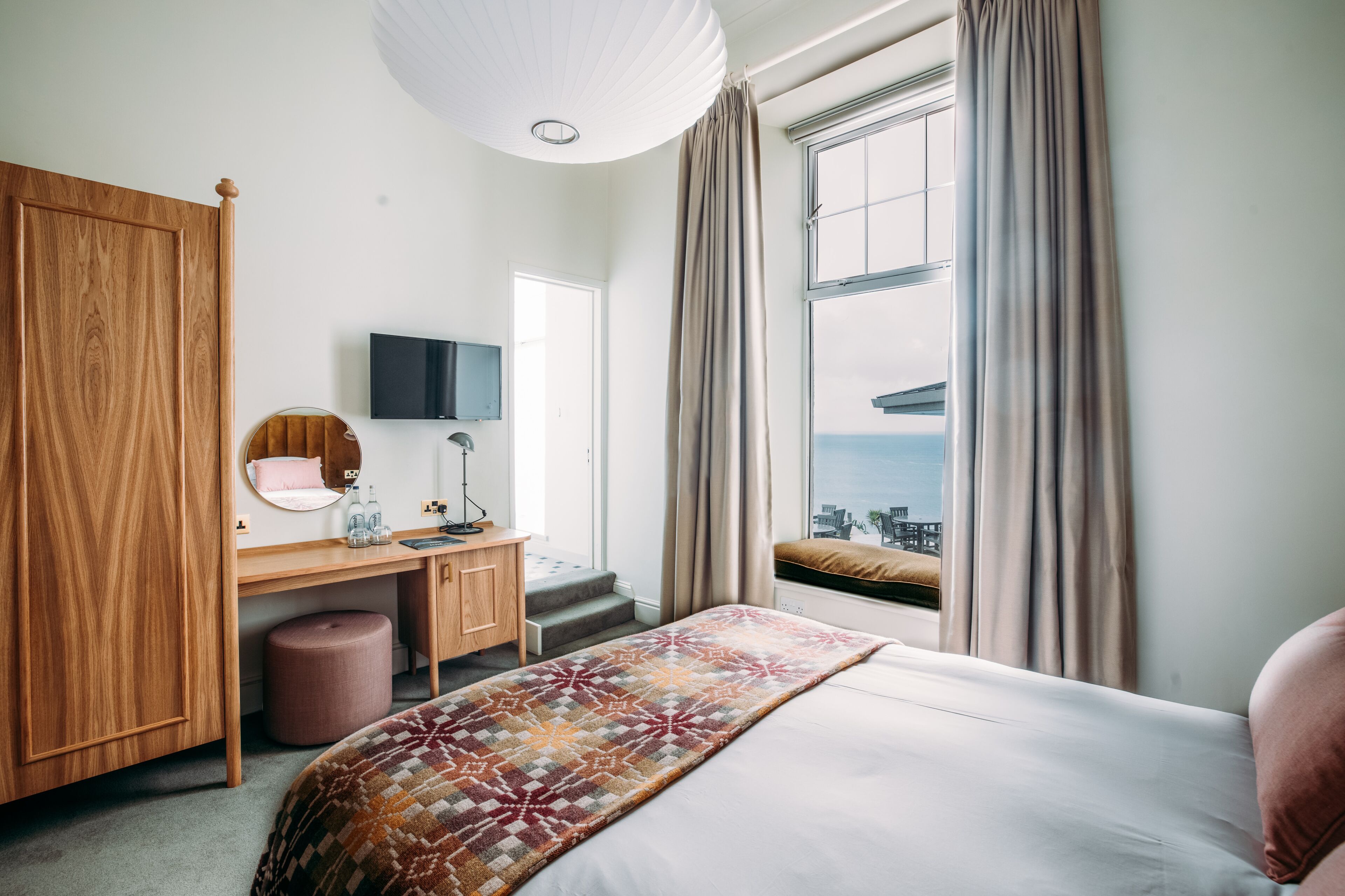 A hotel room with a bed, a desk, a chair, a television, and a window with curtains.
