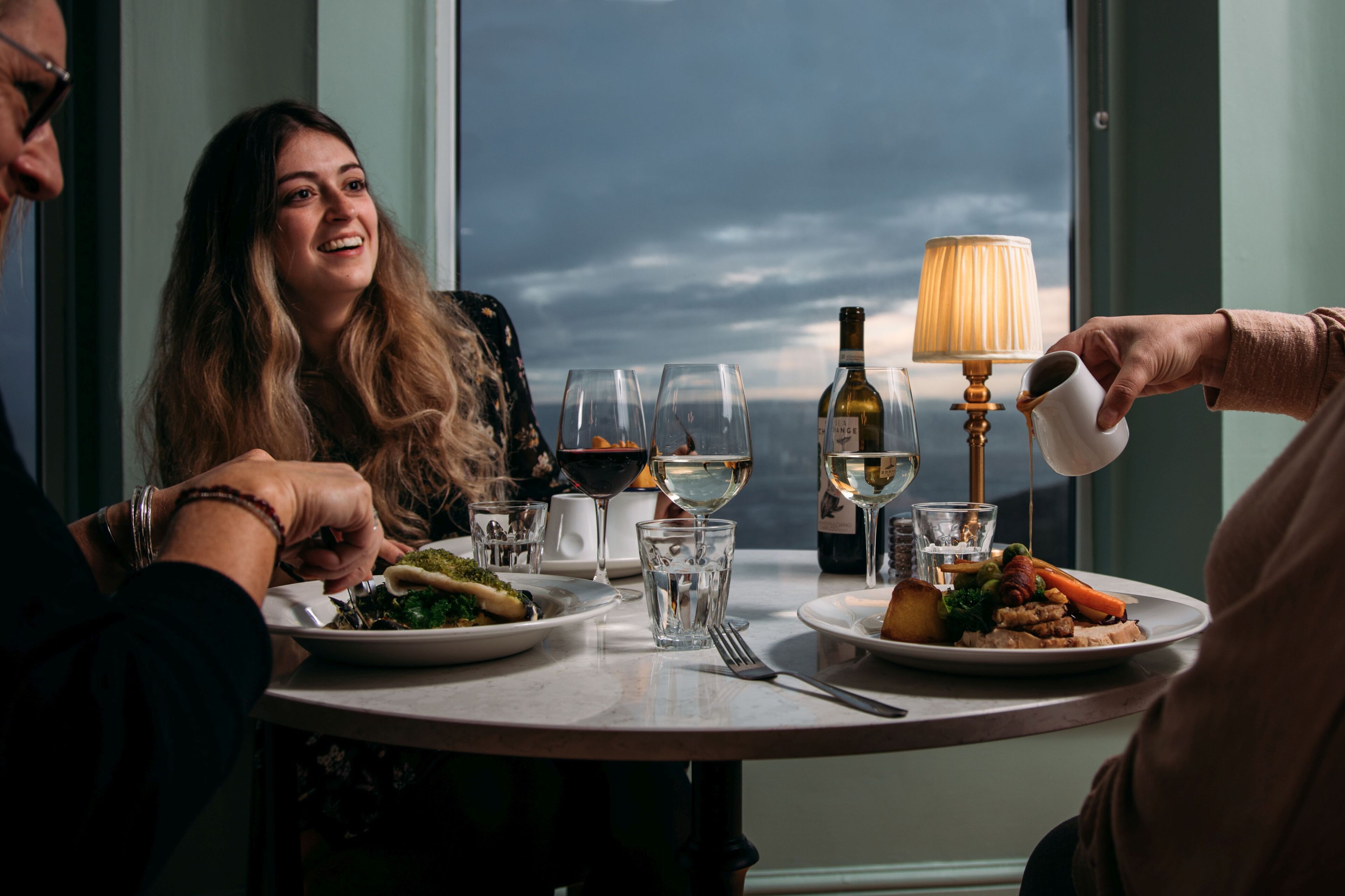 Uma mesa de jantar com pratos de comida, copos de vinho e uma garrafa de vinho.