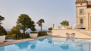 Ein Pool mit freiem Blick auf das Meer, ein Gebäude mit einer Kuppel und ein Balkon mit Geländer.