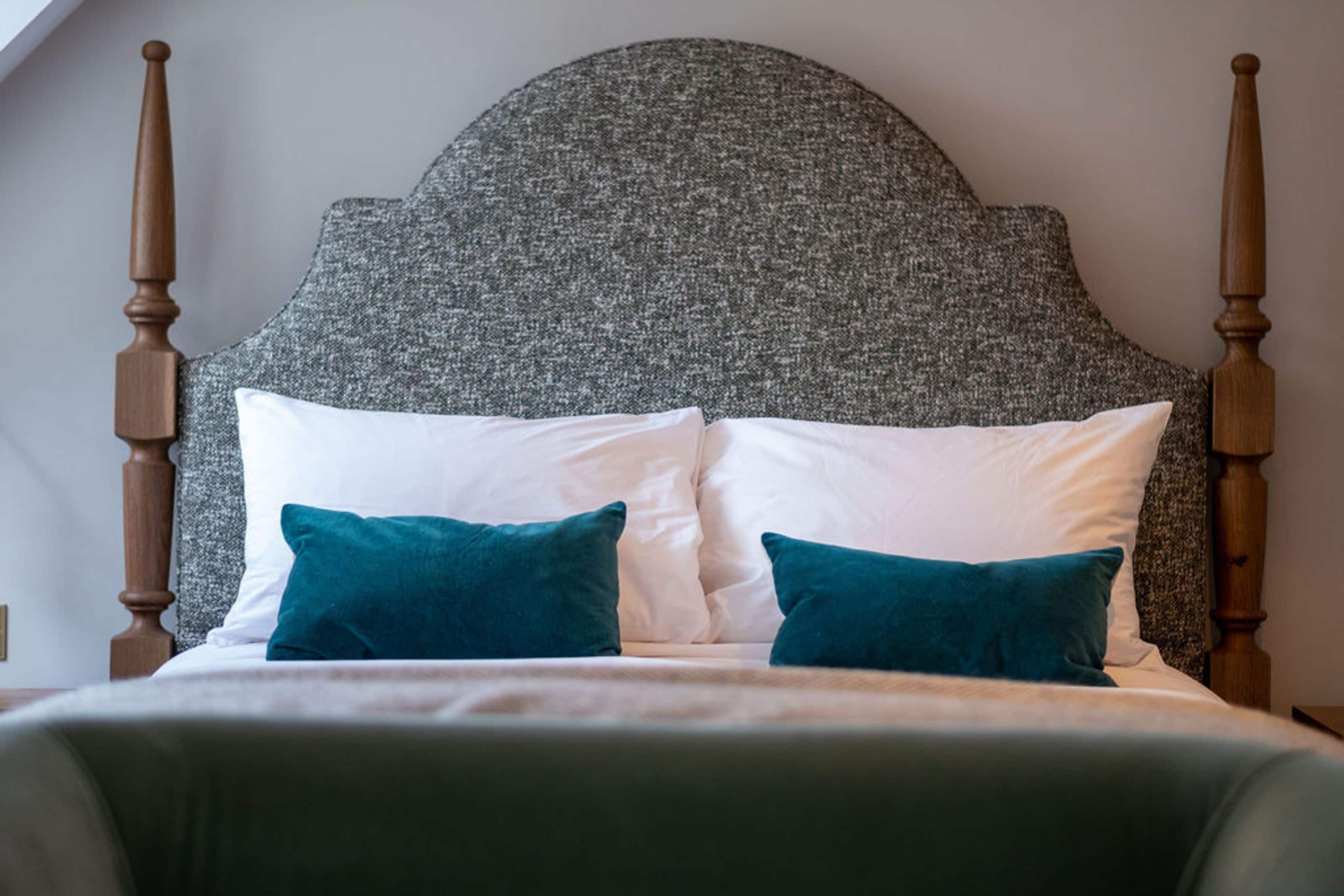 A bed with a grey upholstered headboard, white and teal pillows, and a wooden frame.