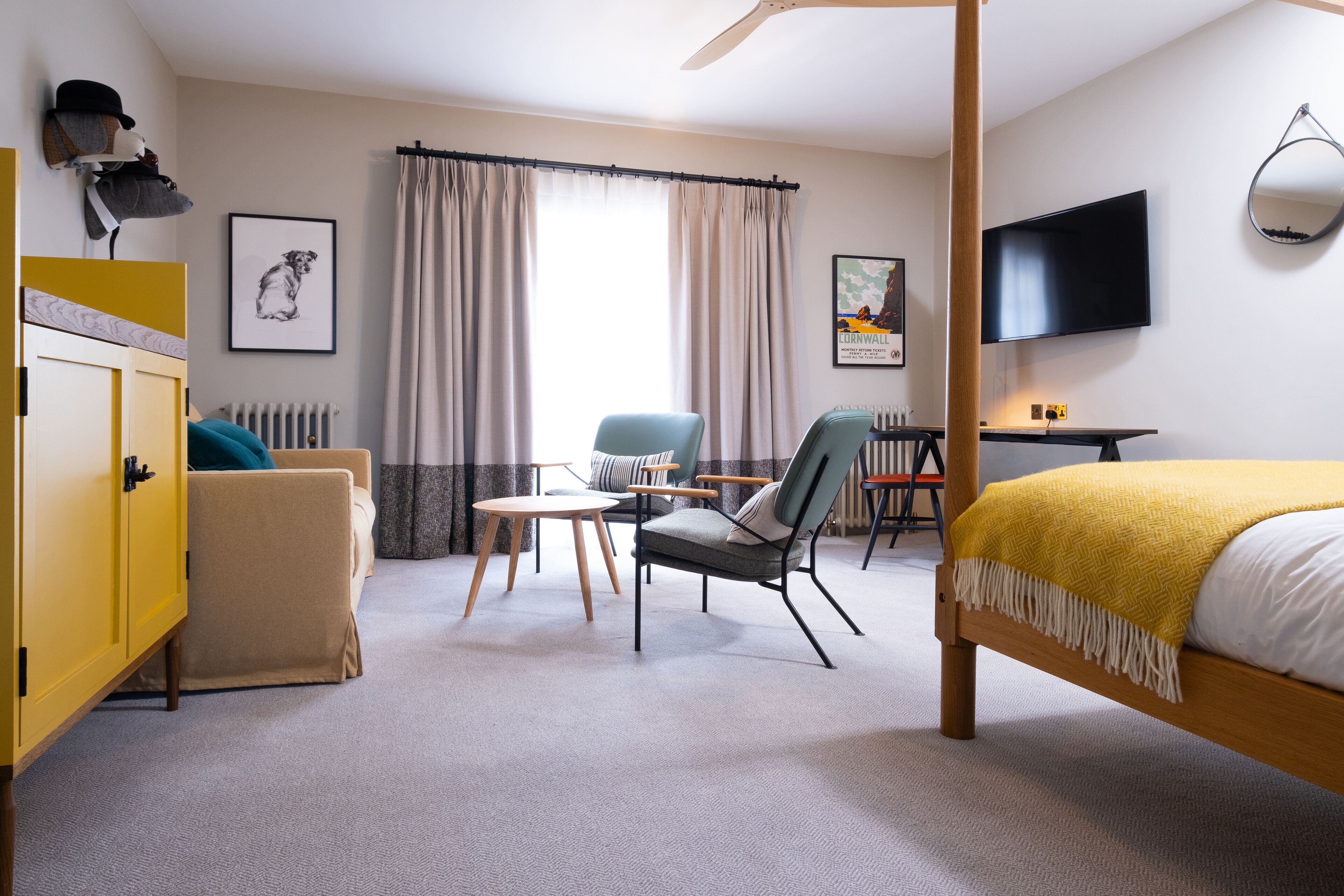 Una habitación de hotel con cama, escritorio, silla, sofá, radiador, televisor y ventana con cortinas.