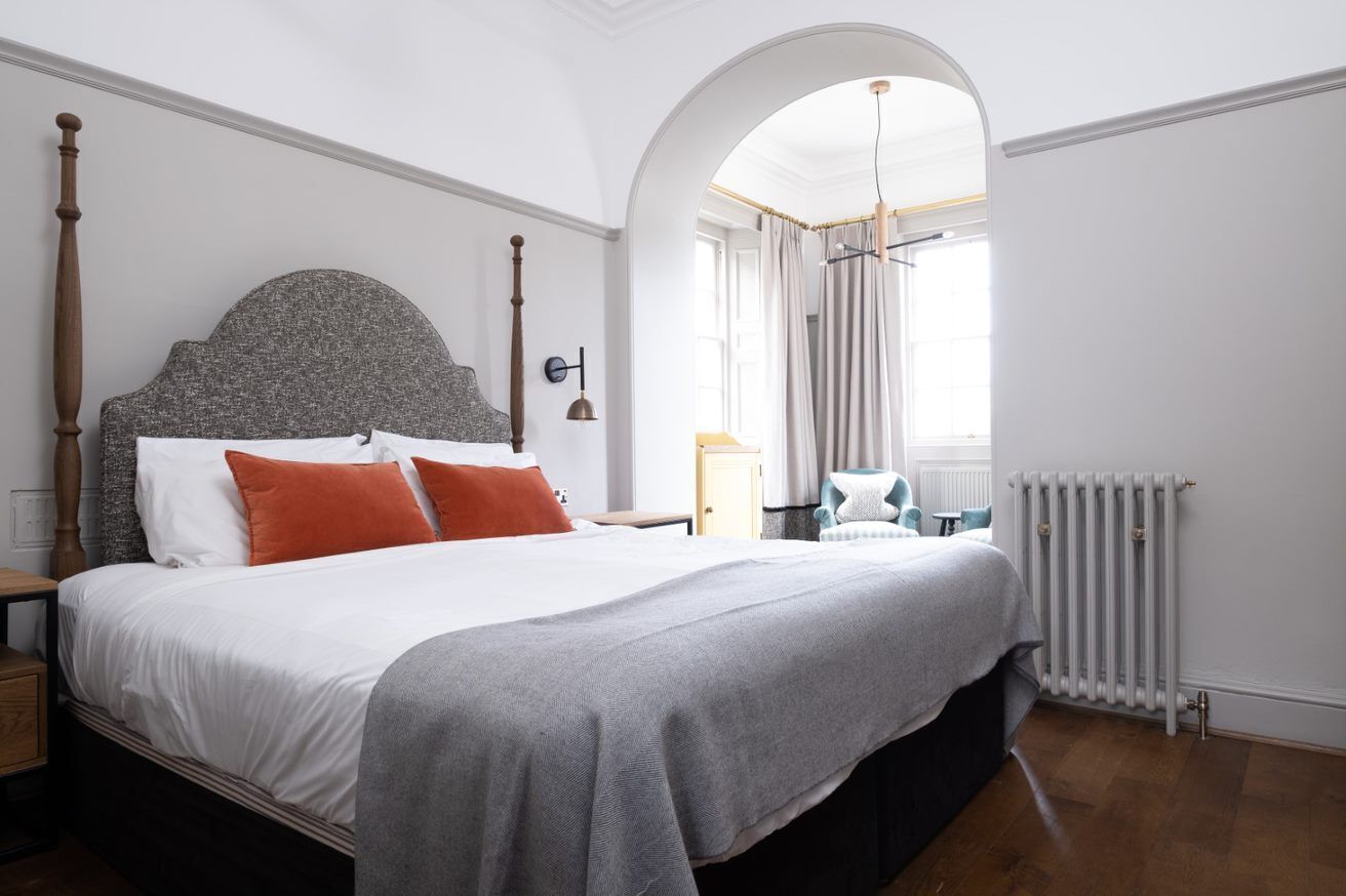 A bedroom with a large bed, a wooden headboard, a nightstand, a chair, and a radiator.