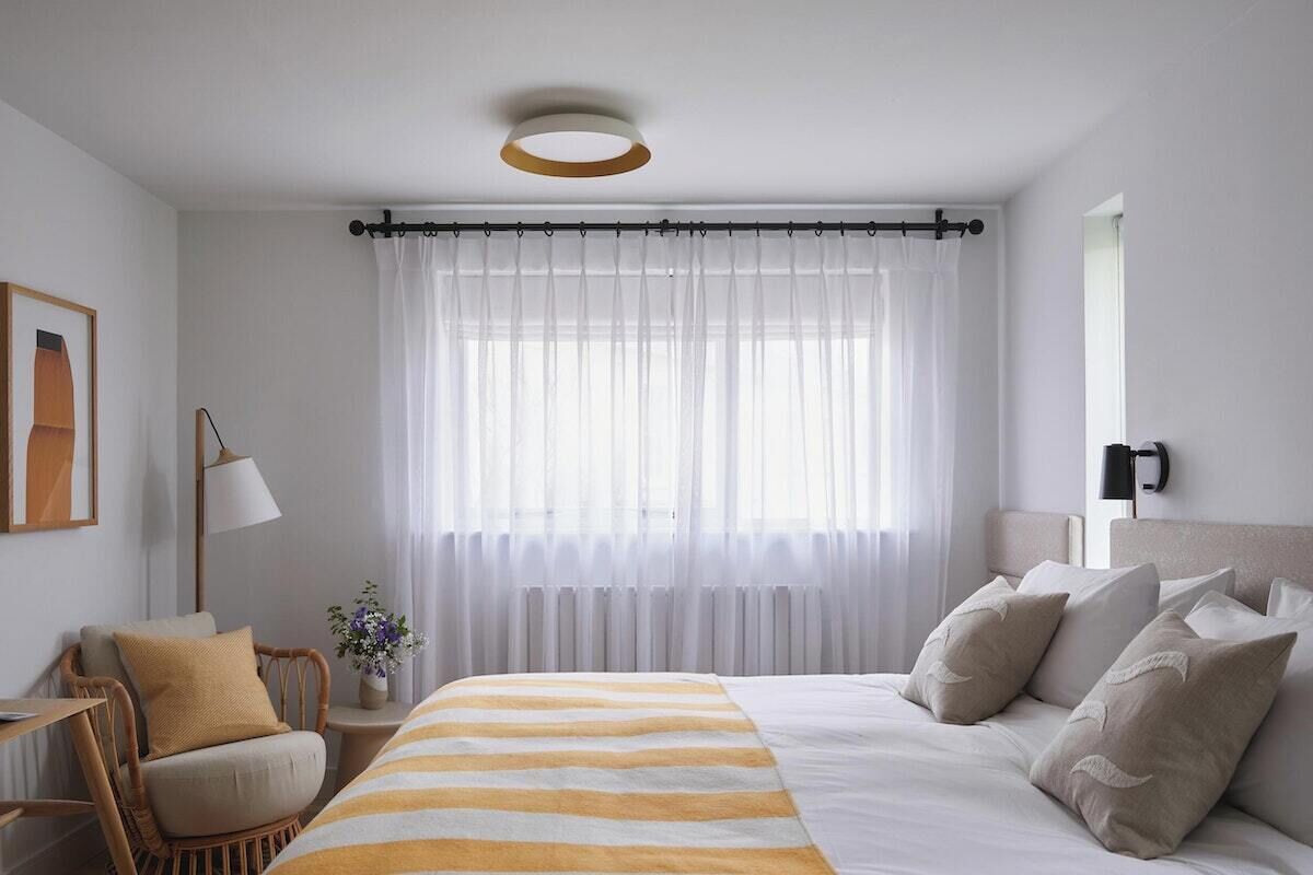 A hotel room with a bed, a chair, a lamp, and a window with curtains.