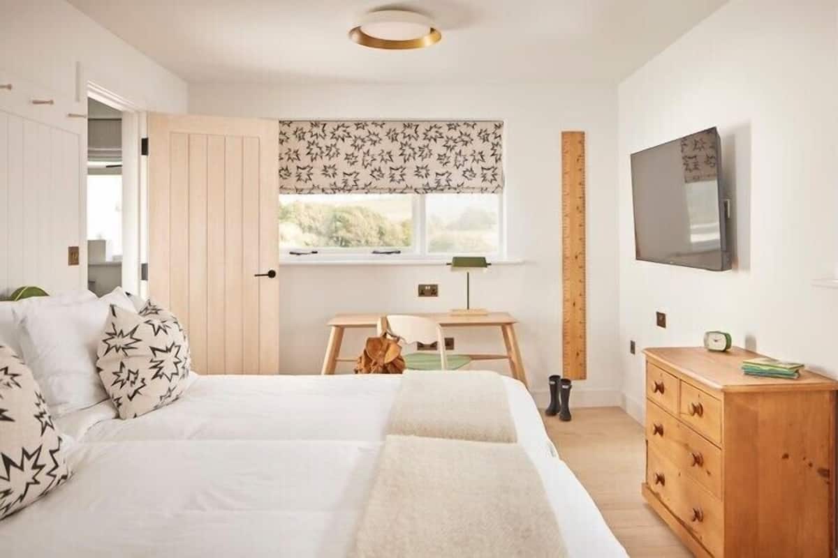 A bedroom with a bed, a desk, a chair, a dresser, a TV, and a window with star-patterned curtains.