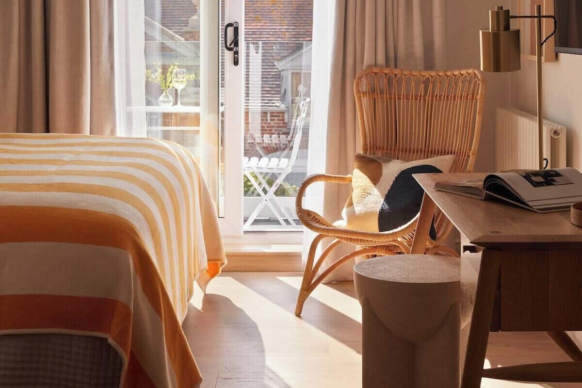 A hotel room with a bed, a wicker chair, a desk, and a view of the outside.
