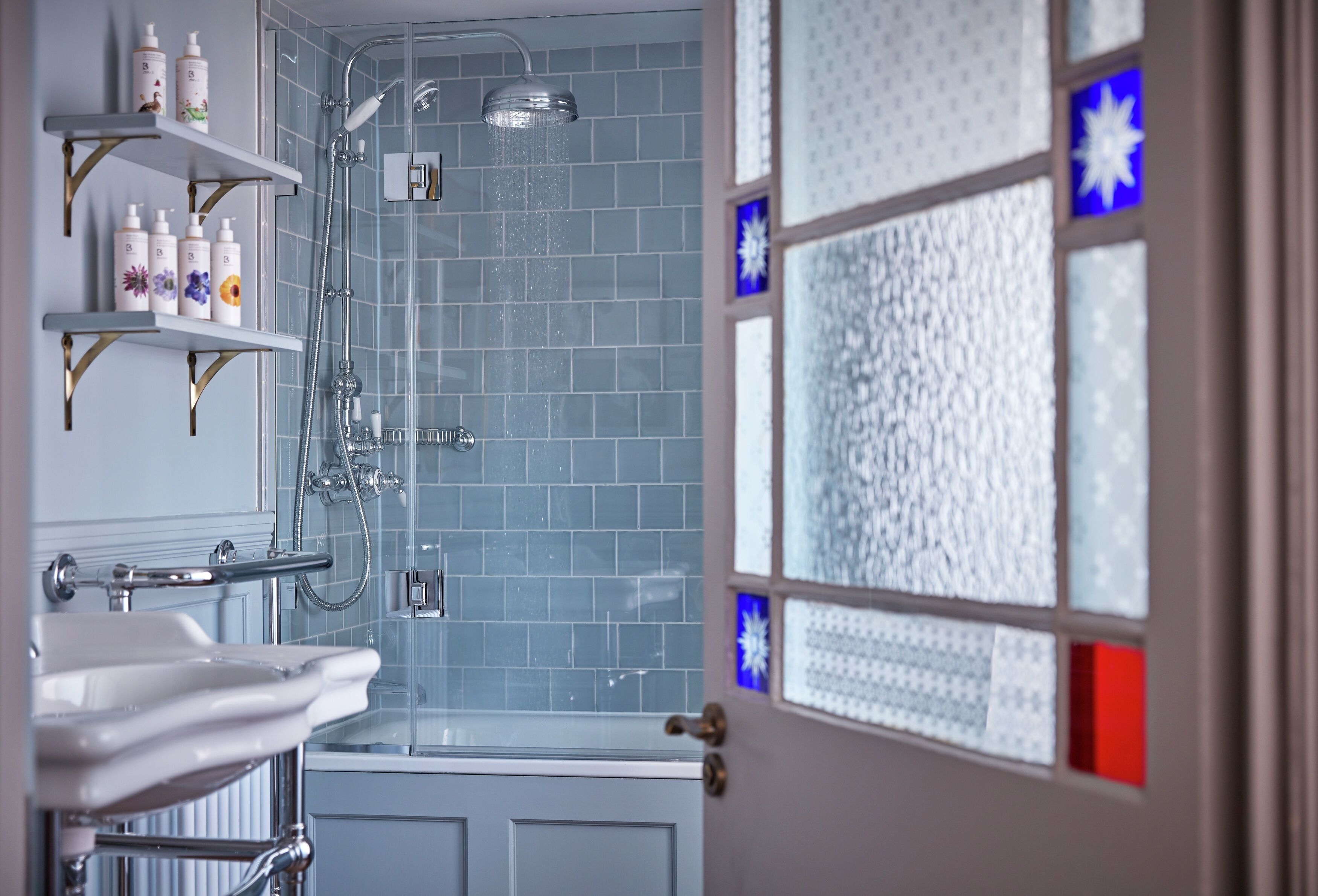 A bathroom with a shower, a sink, and shelves with toiletries.