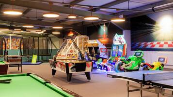 Un espace de loisirs comprenant une table de billard, un baby-foot, des jeux d’arcade et une fresque murale sur le thème de l’espace.