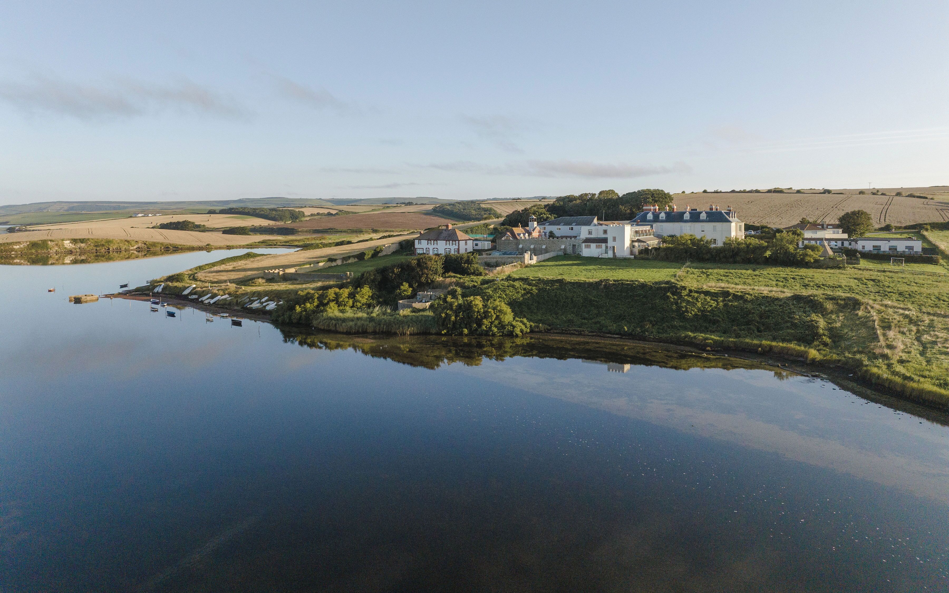 A coastal village with white buildings, a calm lake, and surrounding fields.