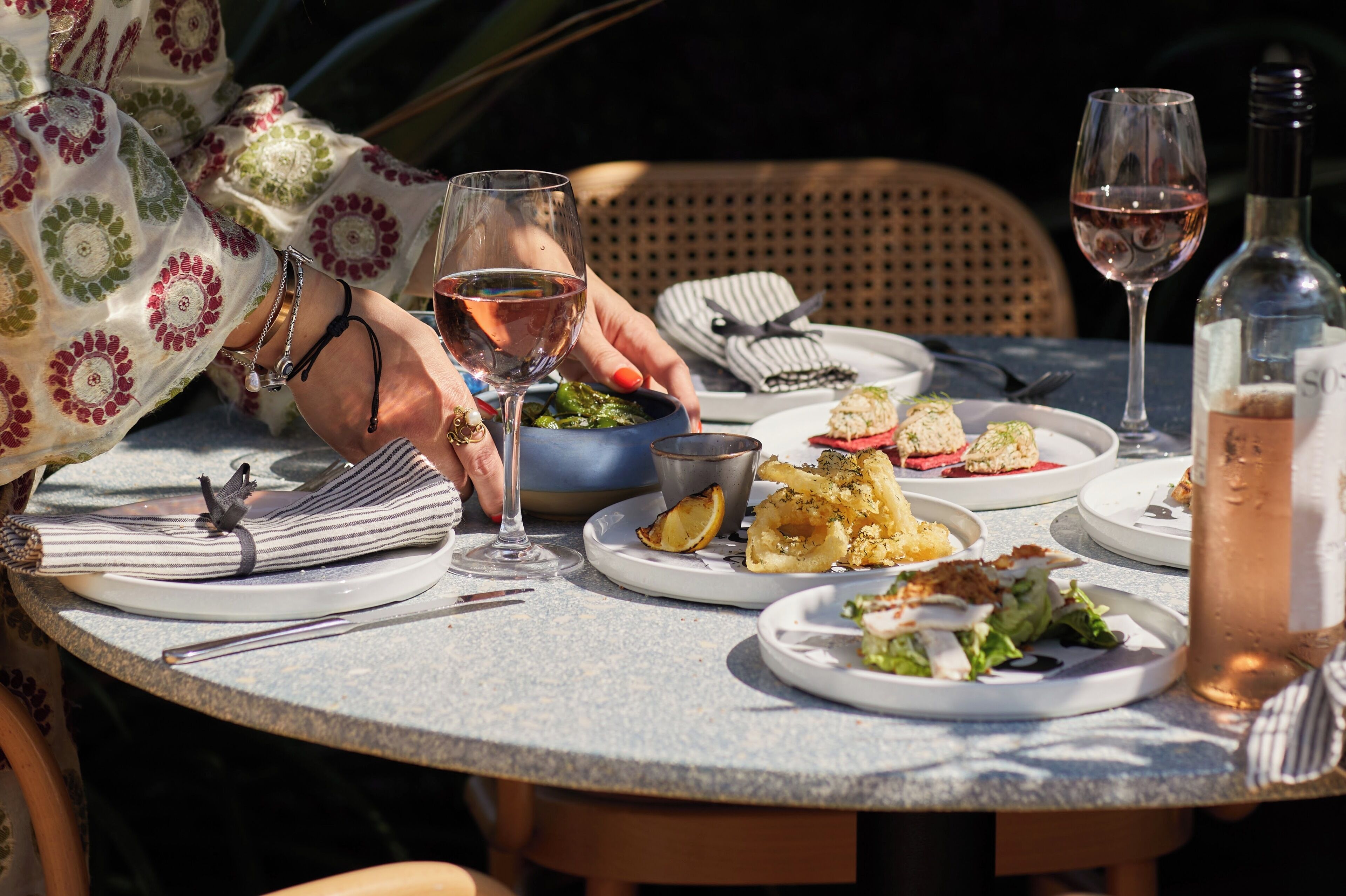 A round table with plates of food, wine glasses, and a bottle.