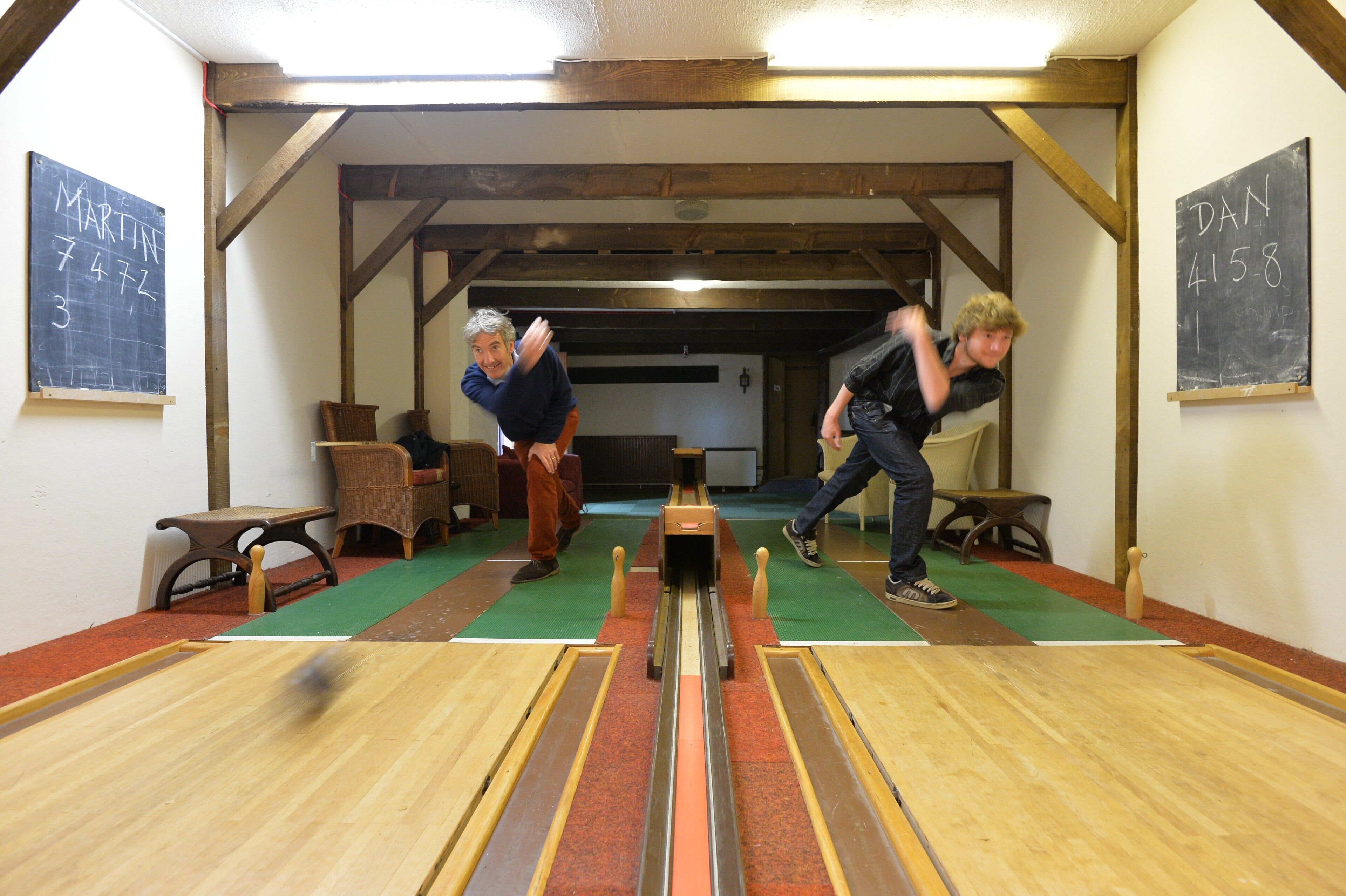 A bowling alley with wooden floors and green carpeted lanes.