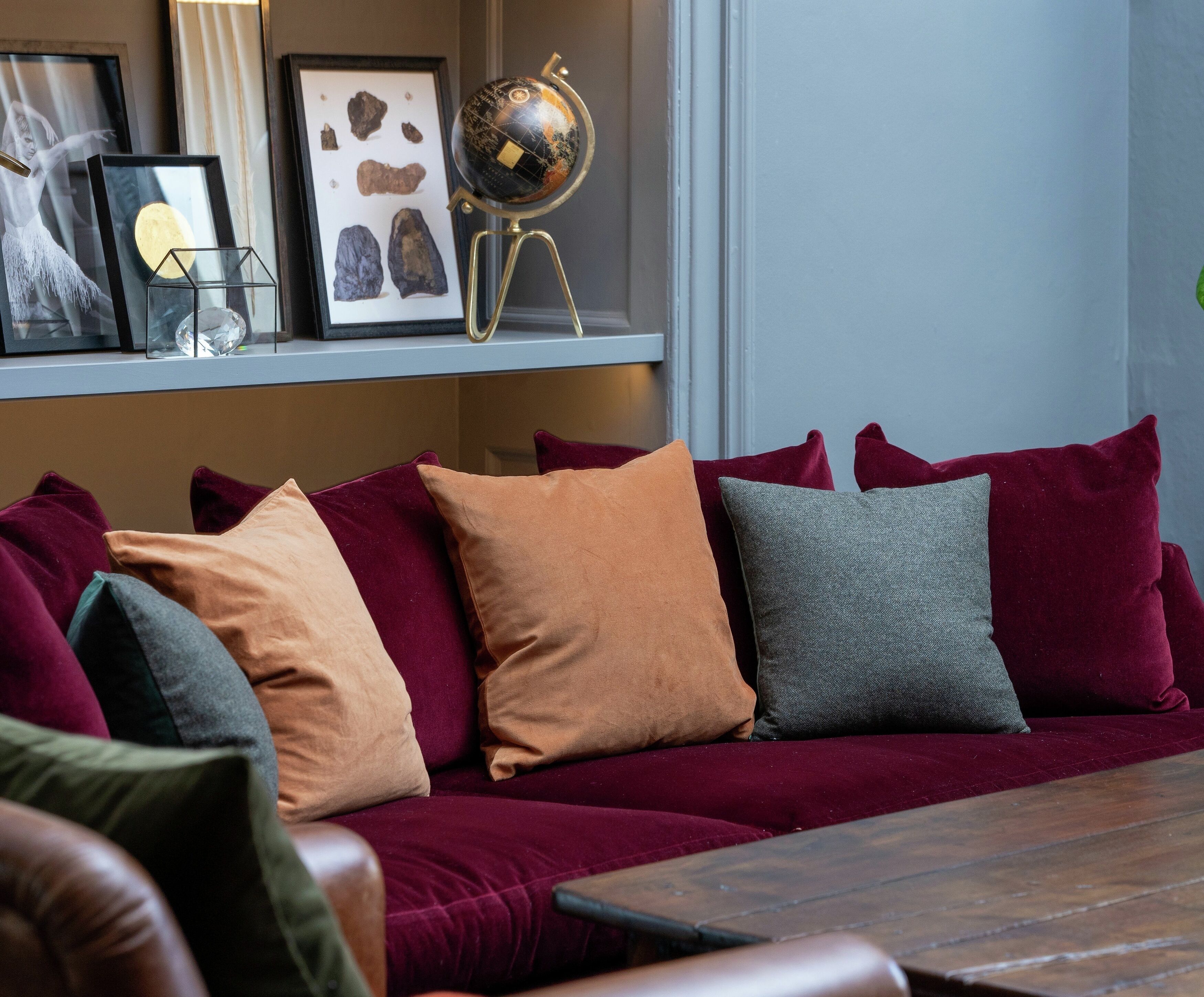 A cozy living room with a red velvet sofa, various cushions, a globe on a stand, and framed artwork on the wall.