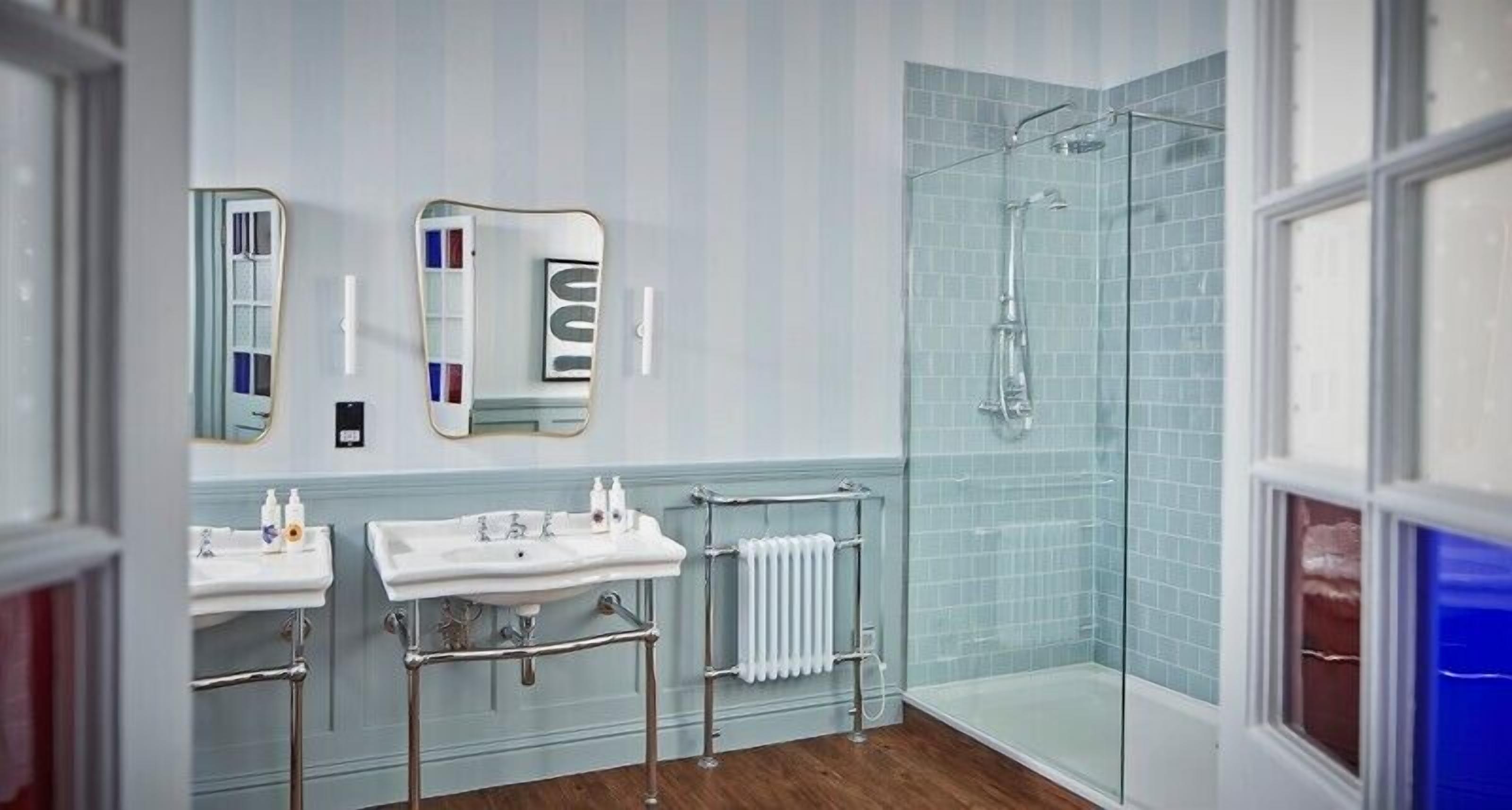 A modern bathroom with two sinks, a glass shower enclosure, and a large mirror.