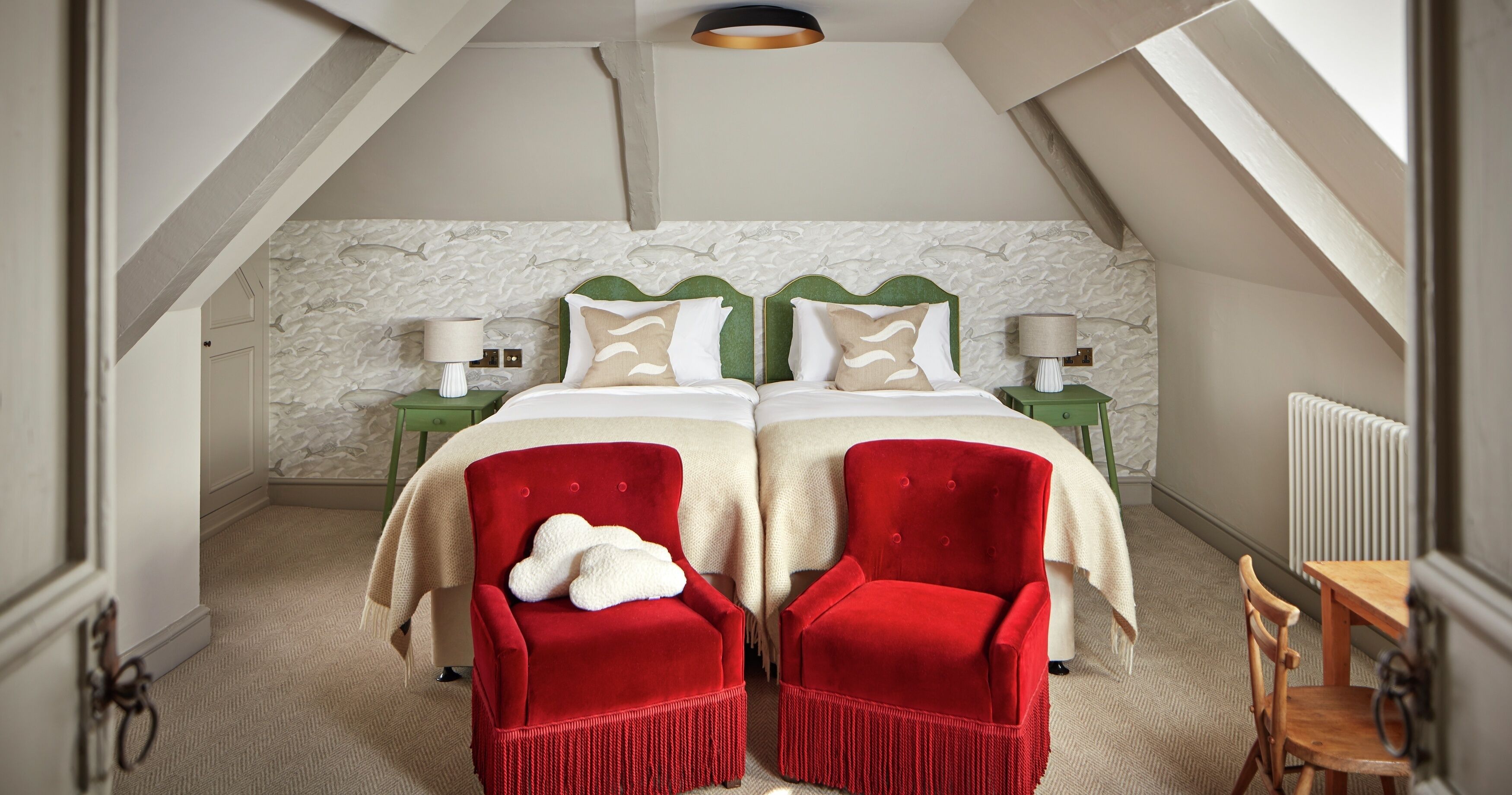 A bedroom with a double bed, two nightstands, a red chair, a wooden chair, and a radiator.