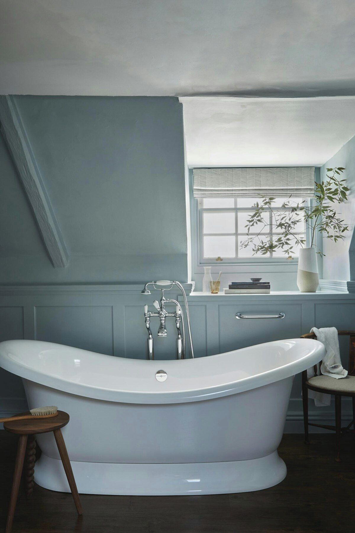 A bathroom with a freestanding bathtub, a window with a view, and a small stool.