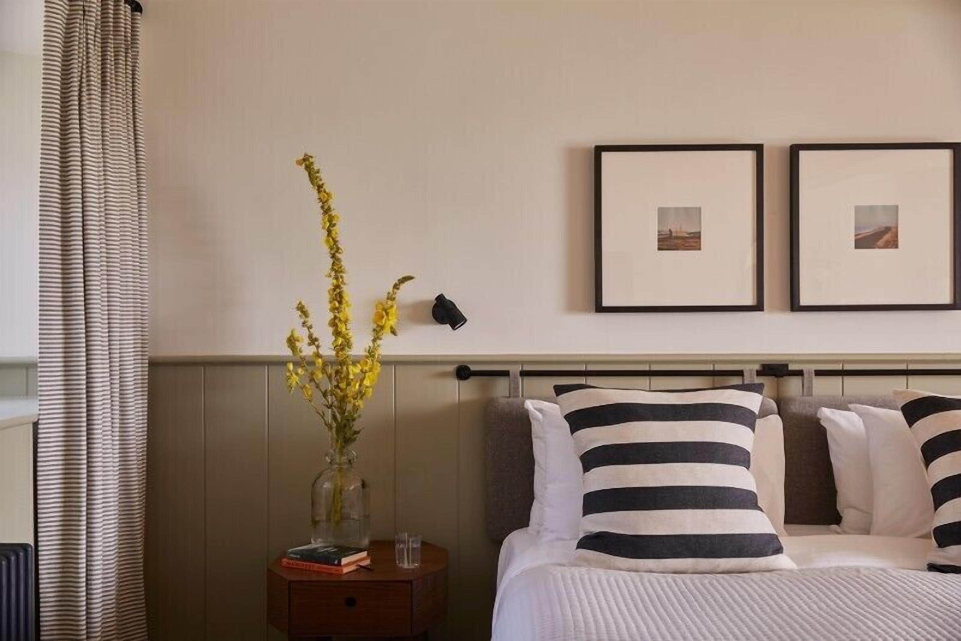 A neatly arranged hotel room with a bed, a bedside table with a vase of flowers, and two framed pictures on the wall.
