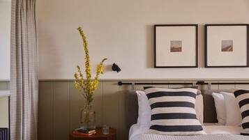 A neatly arranged hotel room with a bed, a bedside table with a vase of flowers, and two framed pictures on the wall.