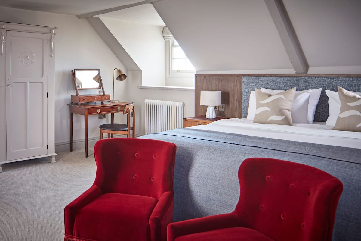 A bedroom with a bed, two red chairs, a dresser, a mirror, and a window.