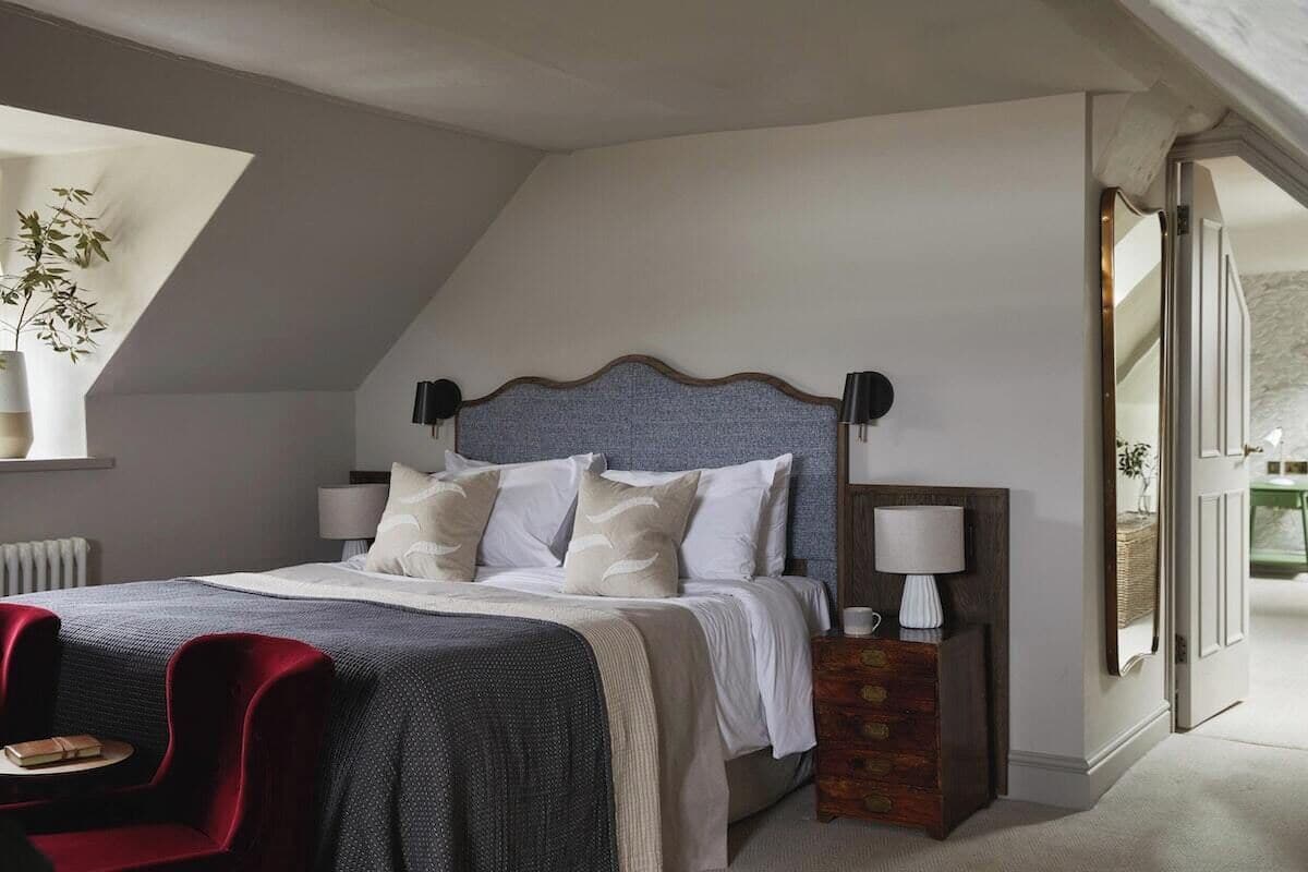 A bedroom with a bed, a red chair, a nightstand, and a lamp.
