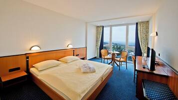 Habitación de hotel con cama, dos sillones, escritorio con televisor y ventana grande con vista a la ciudad.