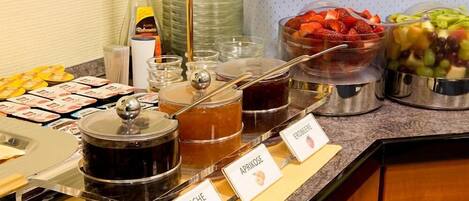 A buffet with labeled containers of apricot, cherry, and raspberry preserves.