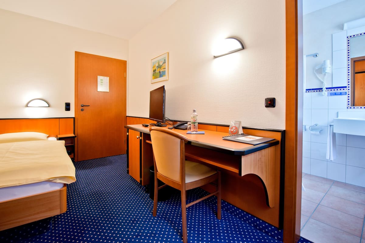 Una camera d'albergo con un letto, una scrivania, una sedia e un bagno con specchio e lavandino.