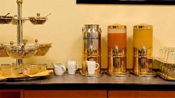 Ein Frühstücksbuffet mit einer Kaffeestation, inklusive Kaffeemaschine, Milchspender und Zuckerlöffel.