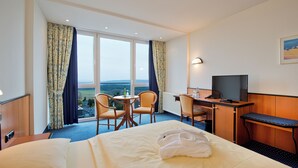Habitación de hotel con cama, escritorio con computadora, dos sillas y vistas al campo.