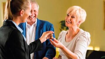 A person in a black suit handing a small object to another person in a white blouse.