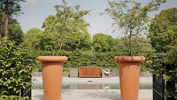 Un área de piscina con dos grandes macetas de terracota, un banco de madera y un muro de piedra al fondo.