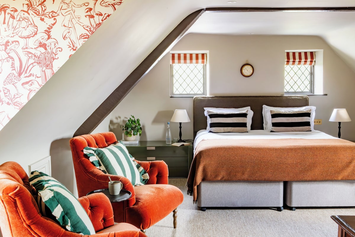A bedroom with a bed, two bedside tables, a nightstand, a chair, and a window with curtains.
