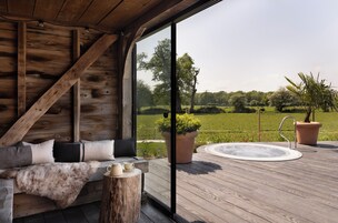 A wooden deck with a hot tub, a seating area with cushions, and a view of a green landscape.