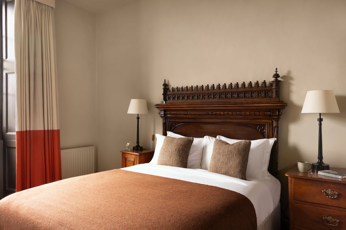 A neatly made bed with a wooden headboard, two bedside tables with lamps, and a window with curtains.