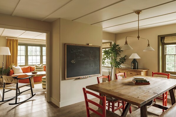 A dining area with a wooden table, red chairs, a blackboard, and a window with curtains.