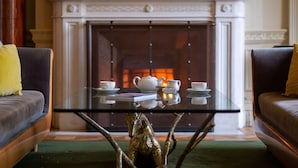 Une pièce avec une cheminée, deux canapés, une table basse en verre avec un pied décoratif et un service à thé.