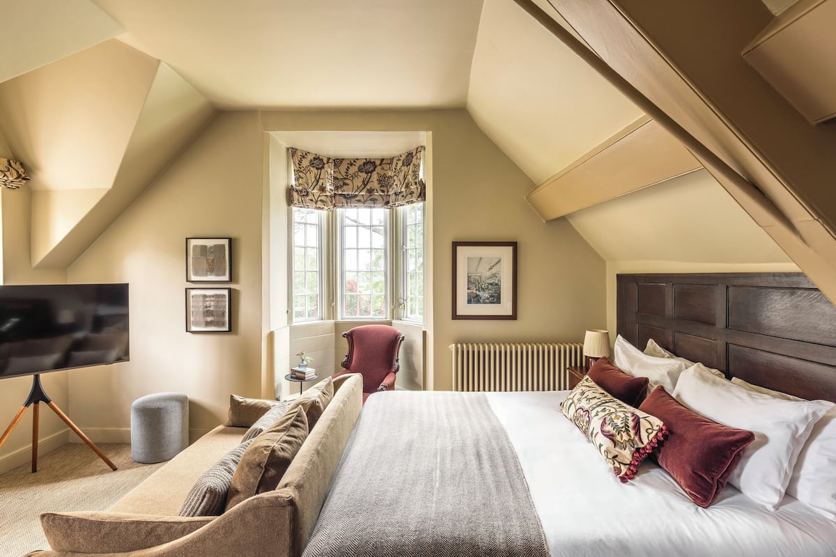 Een slaapkamer met een groot bed, een rode fauteuil, een flatscreen-tv en een raam met gordijnen.