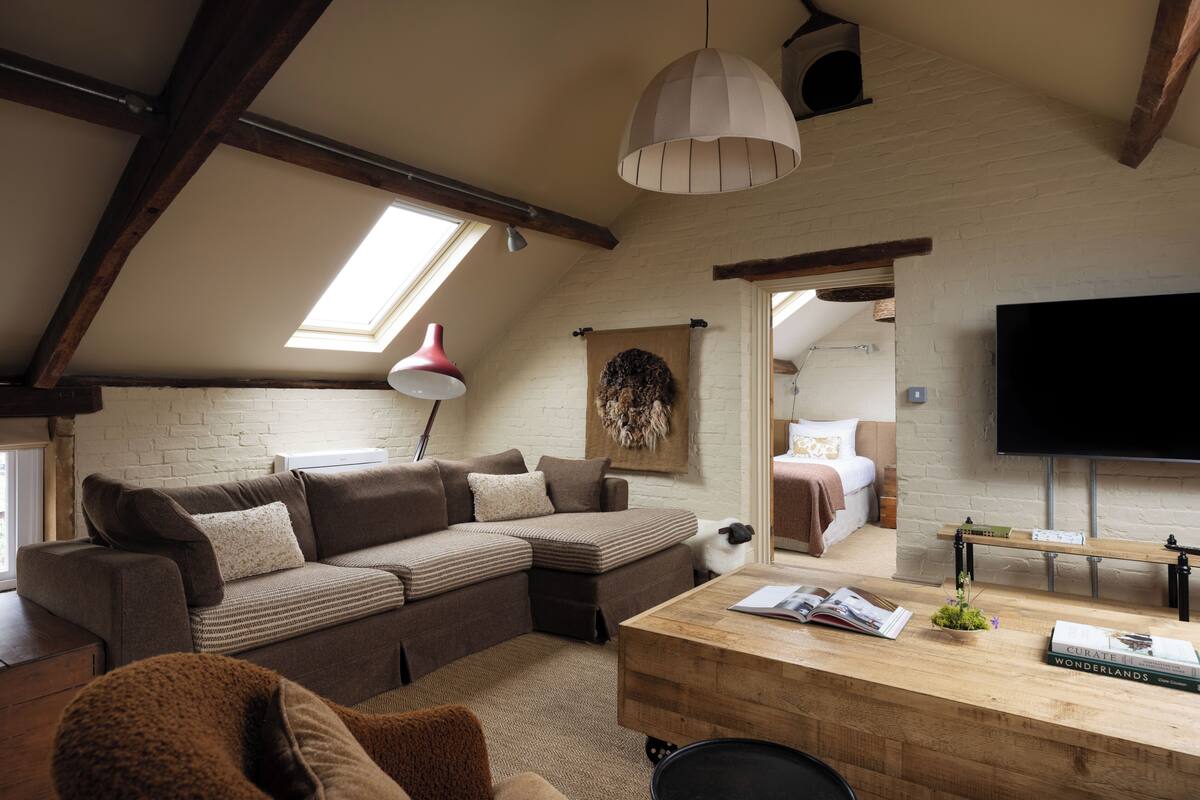 Een loft-stijl kamer met een hoekbank, een houten bureau, een flatscreen-tv en een dakraam.