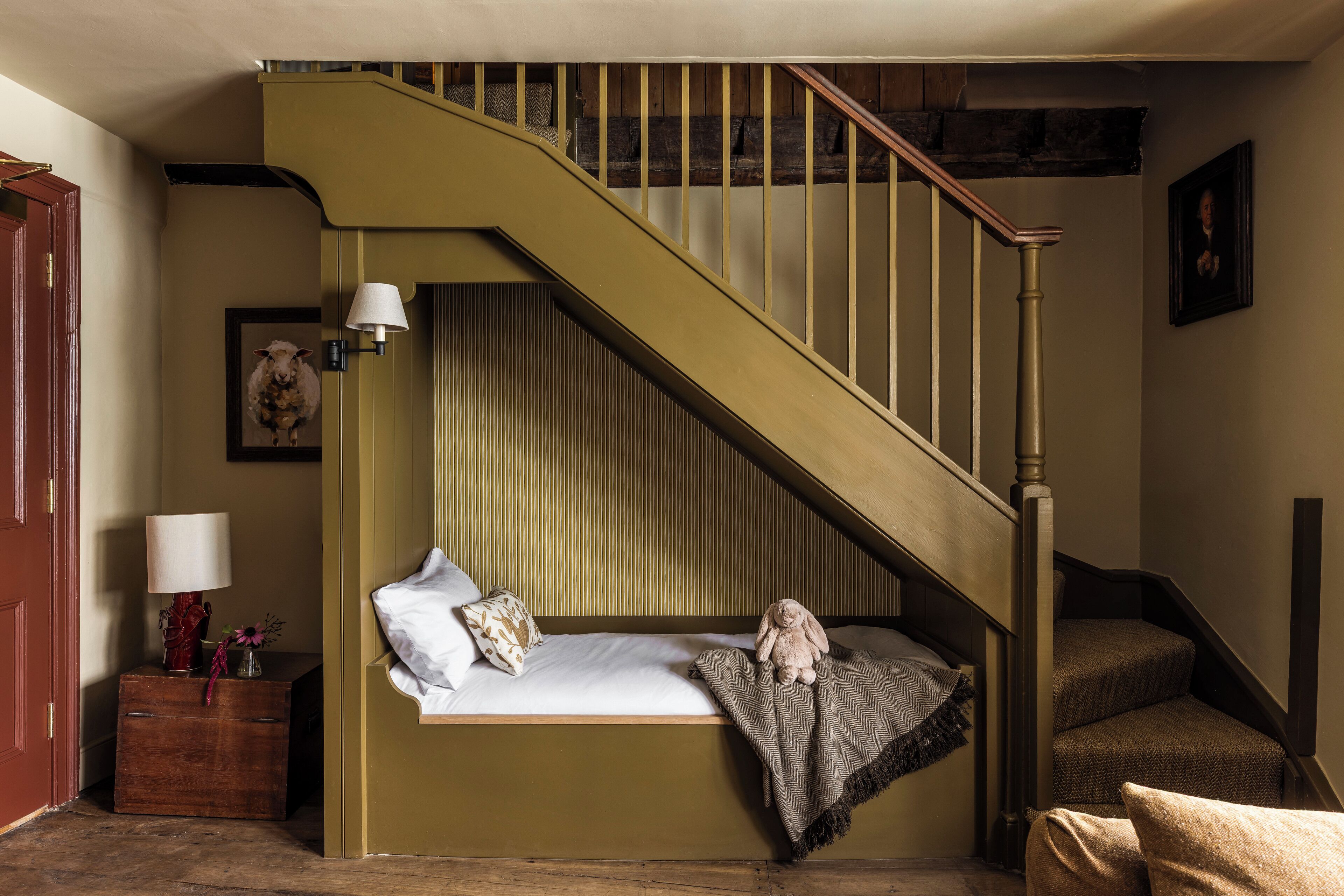 A bedroom with a bed, a nightstand, a lamp, a framed picture, and a staircase.