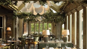 A restaurant with tables set for dining, large lamps, and a ceiling adorned with greenery.