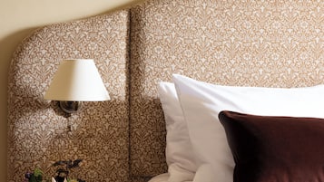 A neatly made bed with white and brown pillows, a small bedside table with a lamp, and a vase with flowers.