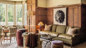A cozy living room with a wooden panel wall, a large window, and a fireplace.