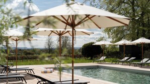 A poolside area with lounge chairs and umbrellas, a pool, and a view of the landscape.