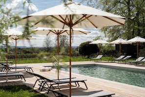 A poolside area with lounge chairs and umbrellas, a pool, and a view of the landscape. - Woolley Grange Hotel (Bradford-on-Avon)