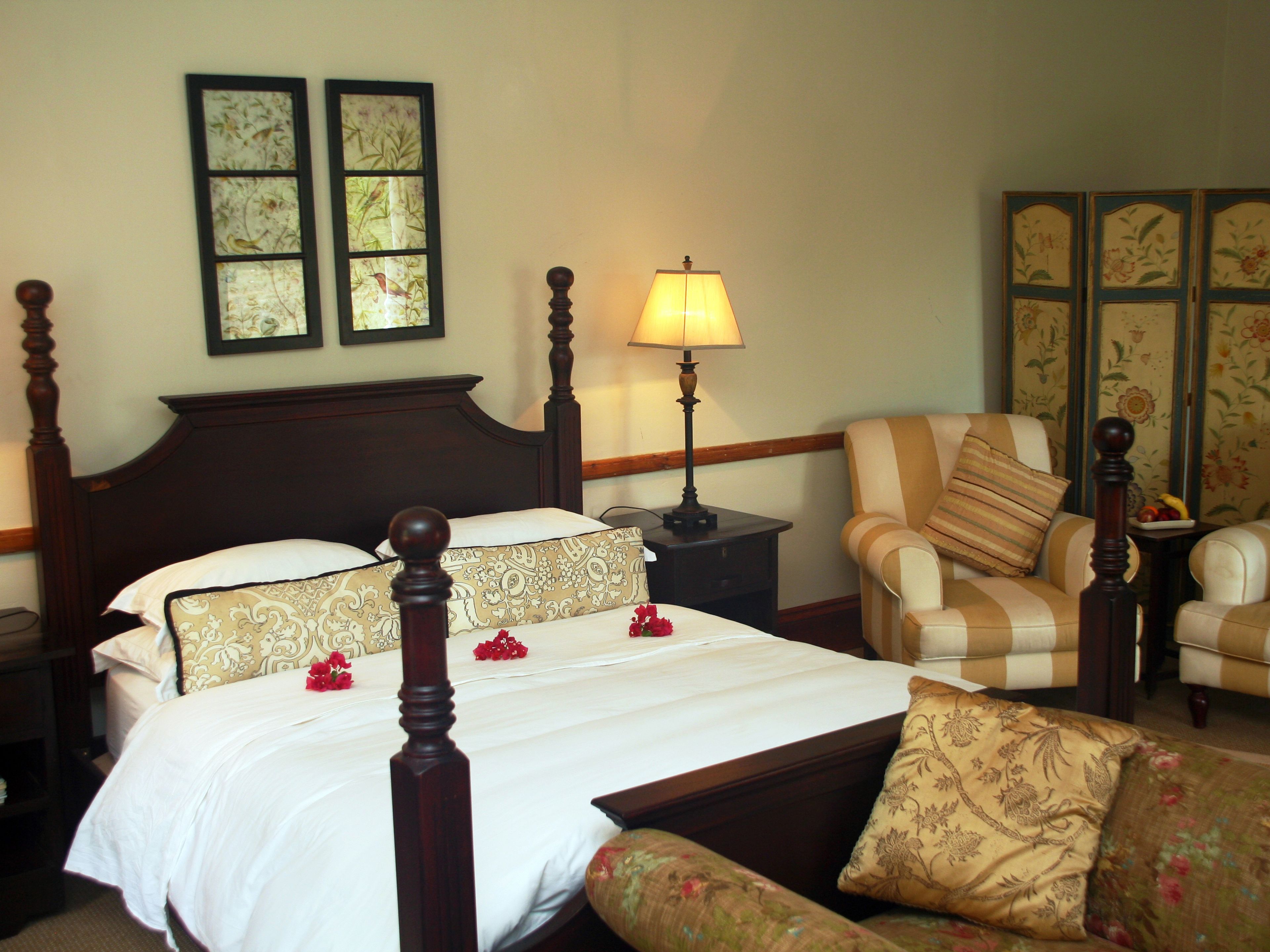 Quarto de hotel com uma cama de dossel, mesa de cabeceira com abajur, poltrona listrada e sofá estampado com flores.